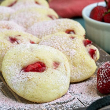 My strawberry shortcake cookies on a wooden plank with strawberry-powdered sugar sprinkled on top.