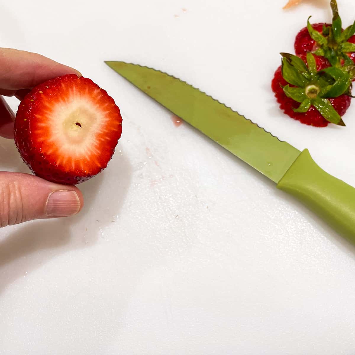 Cutting top off of a strawberry to show the center that will be hulled.