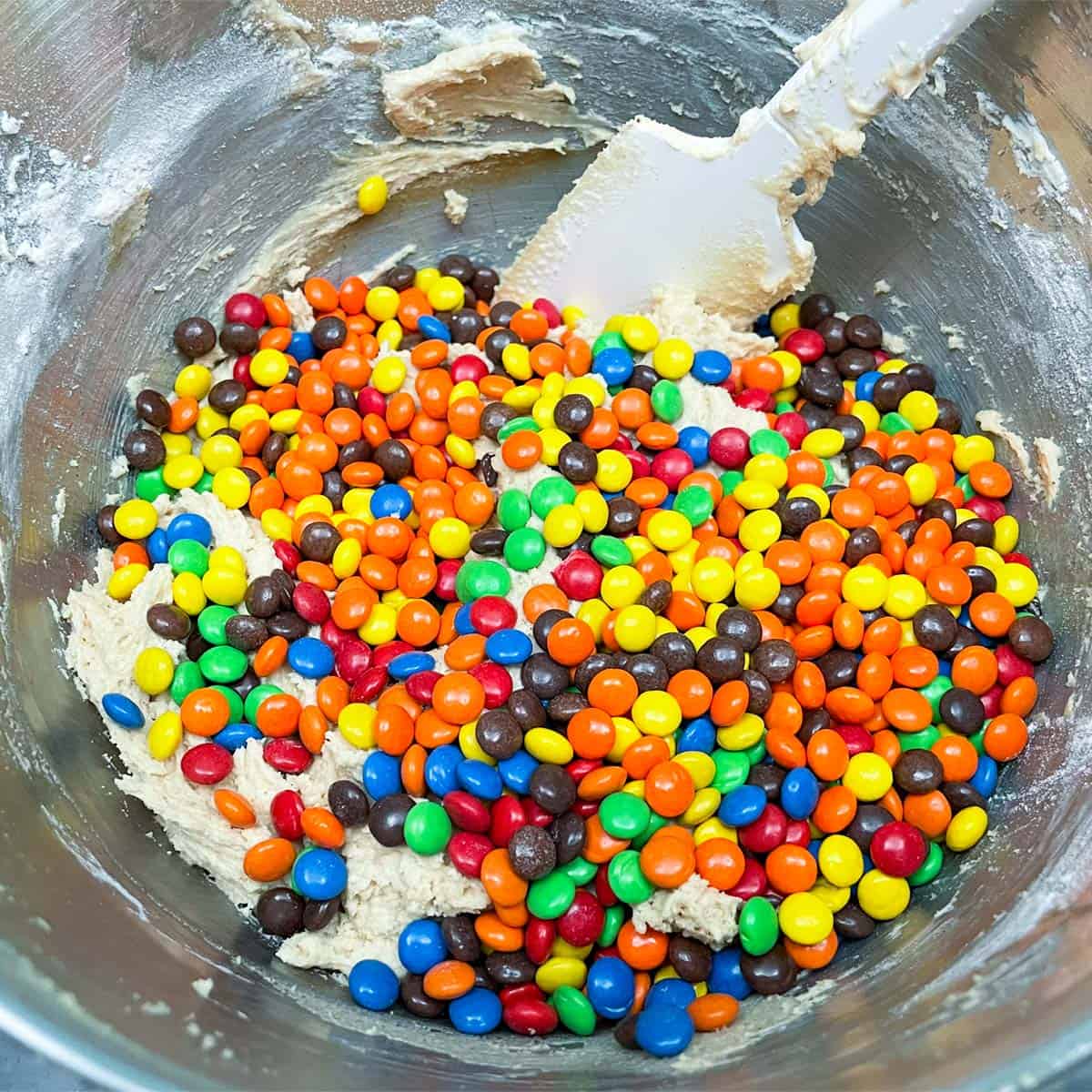 Mini M&M's along with Reese's mini pieces are added to the bowl of the peanut butter cookie dough.