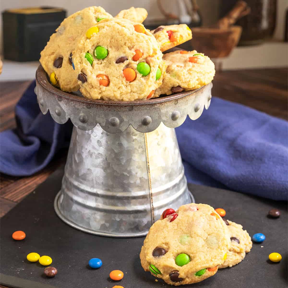 Peanut butter M&M cookies on a black board and stacked on a pewter stand.