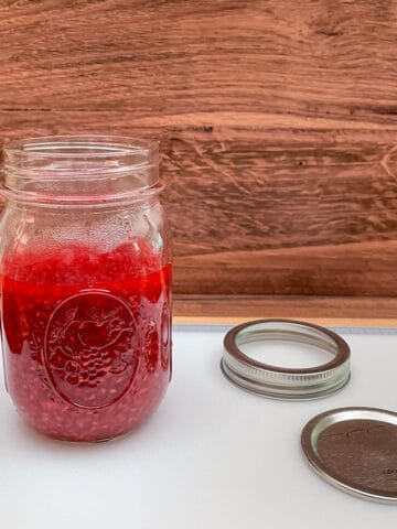 Warm Raspberry Jam in a glass container to finish cooling before adding a lid and placing it into the refrigerator.