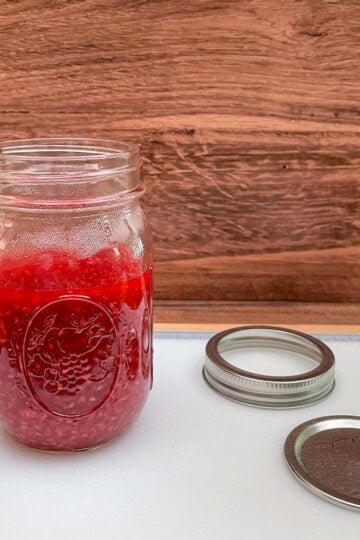 Warm Raspberry Jam in a glass container to finish cooling before adding a lid and placing it into the refrigerator.