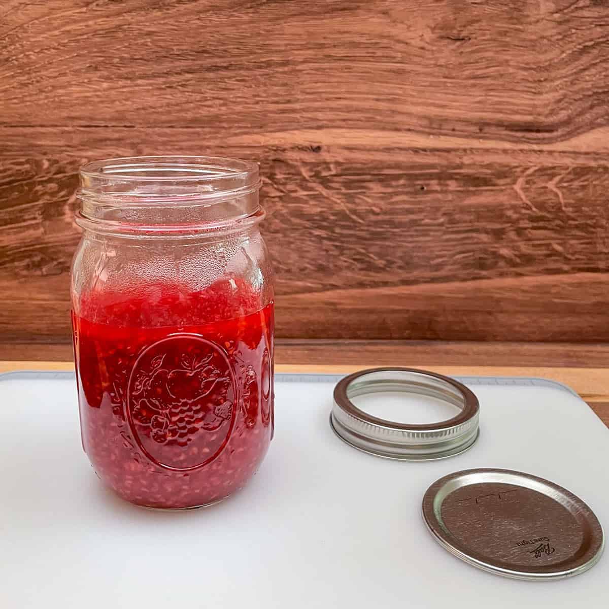 Warm Raspberry Jam in a glass container to finish cooling before adding a lid and placing it into the refrigerator.