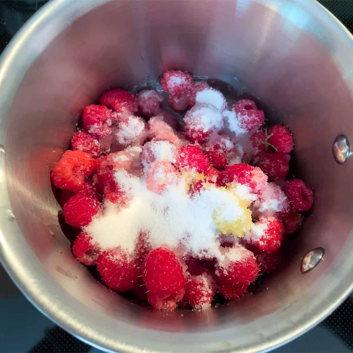 Raspberries, sugar, and lemon zest added to a small saucepan.