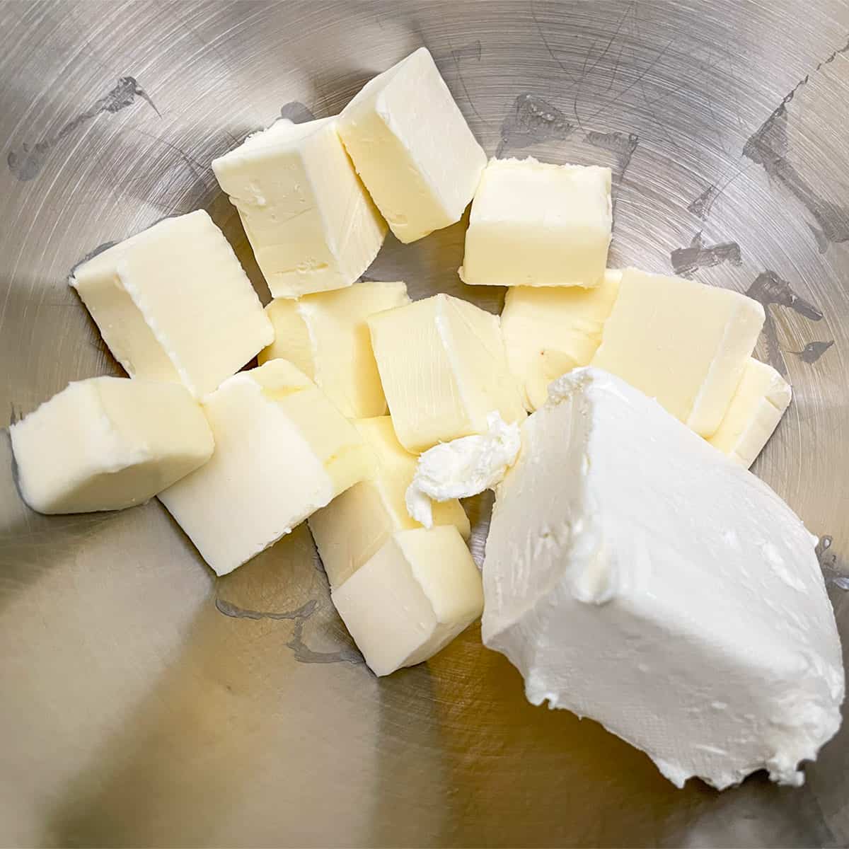 Cubed butter and a block of cream cheese ready to be mixed in a mixer bowl.