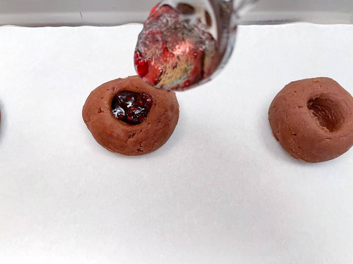 Filling a chocolate jam cookie with raspberry jam.