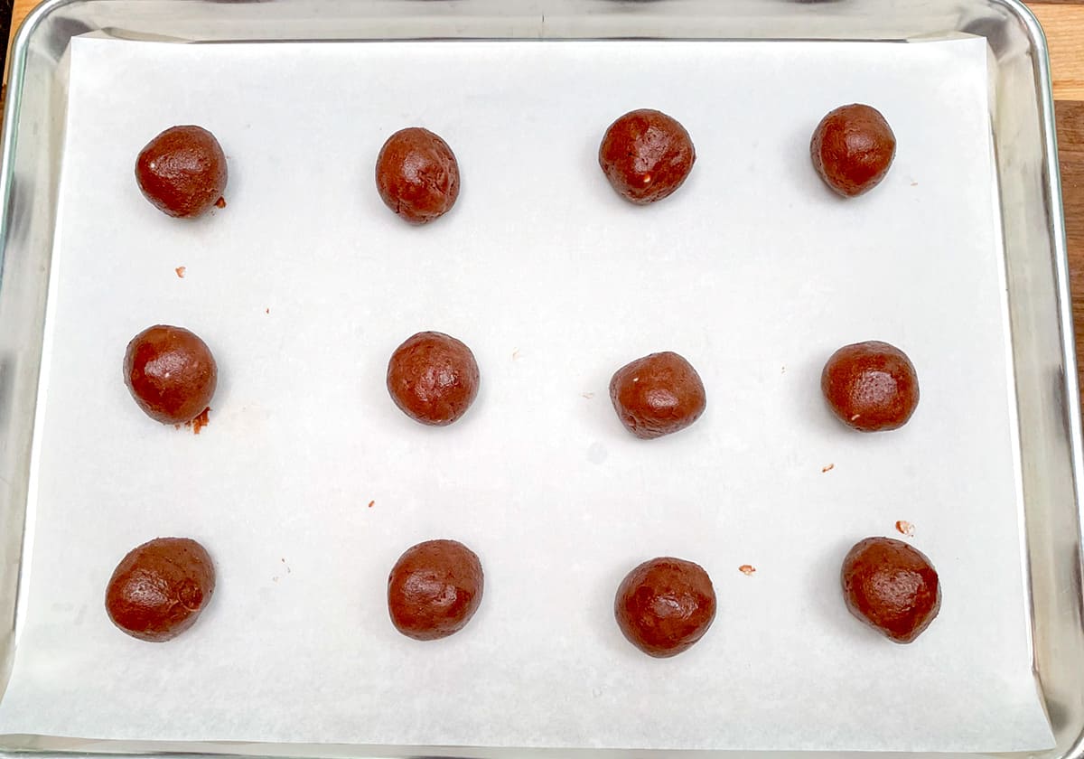Twelve chocolate rolled balls on a sheet pan.