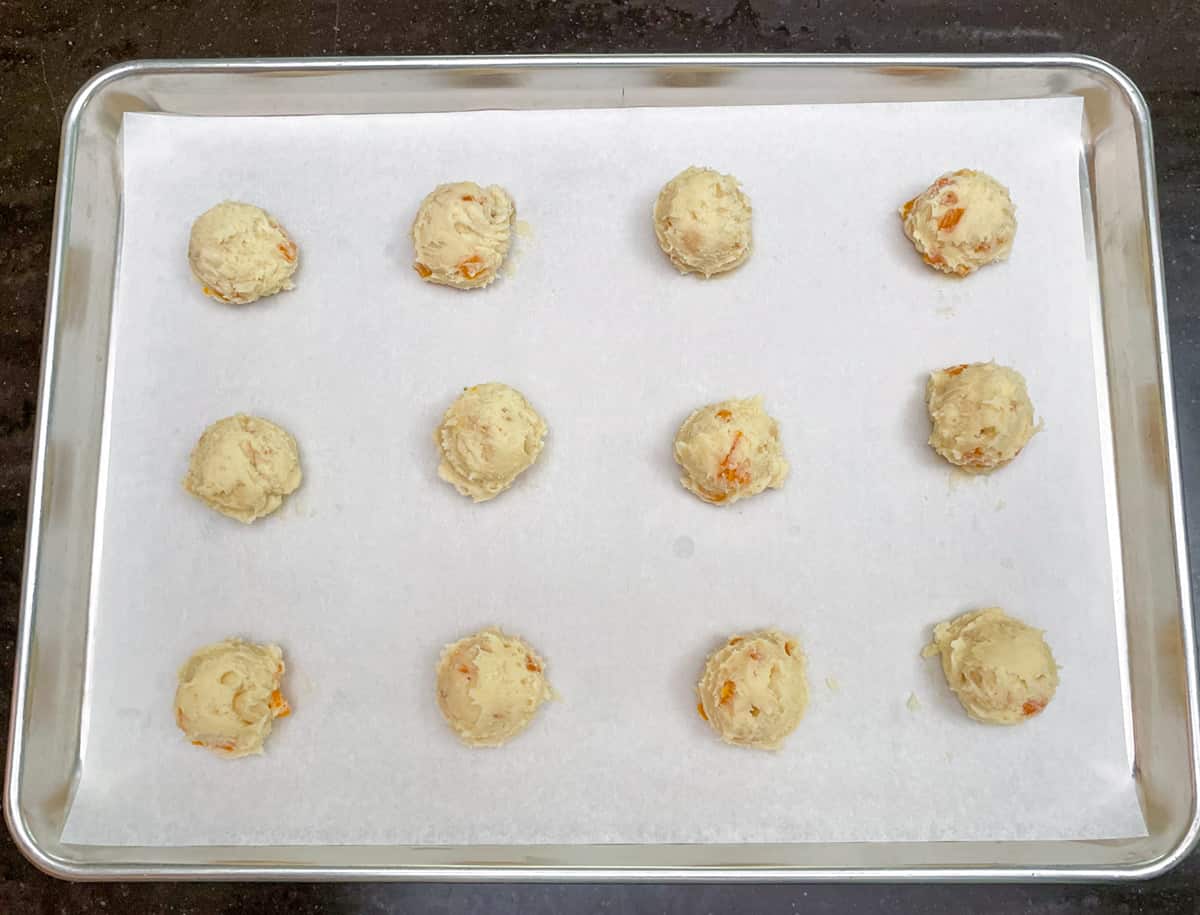 Scooped cookie dough on parchment-lined sheet baking pan.