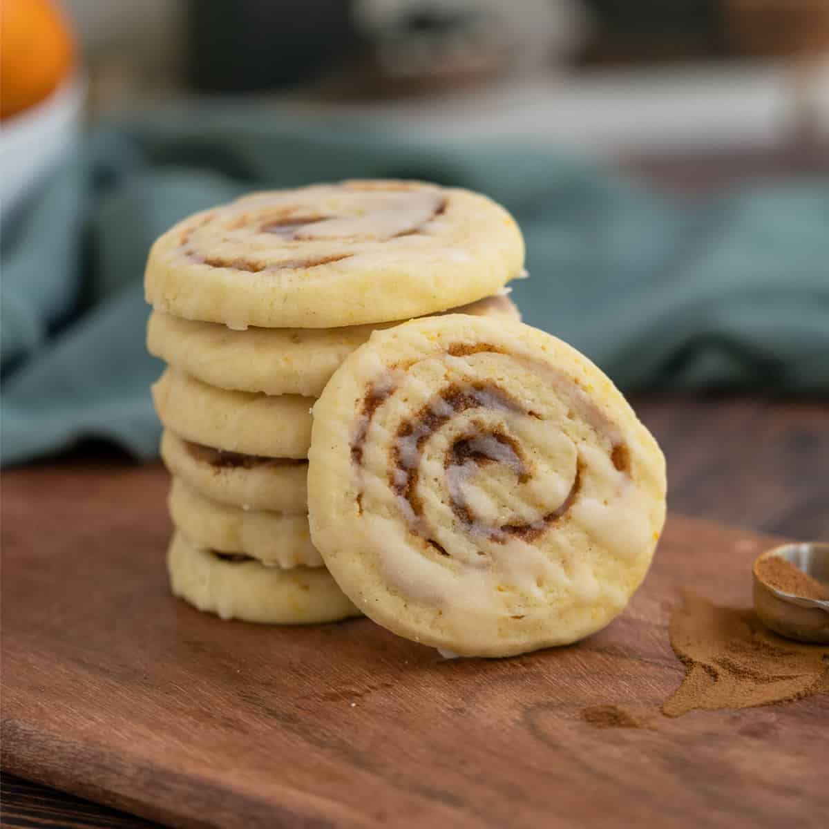 Stack of cinnamon orange pinwheel cookies with one facing front and on a wooden plank.