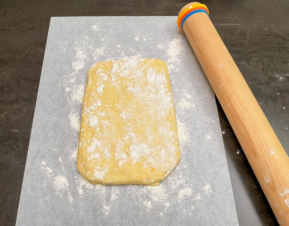 Cookie dough on a sheet of parchment paper with a rolling pin.