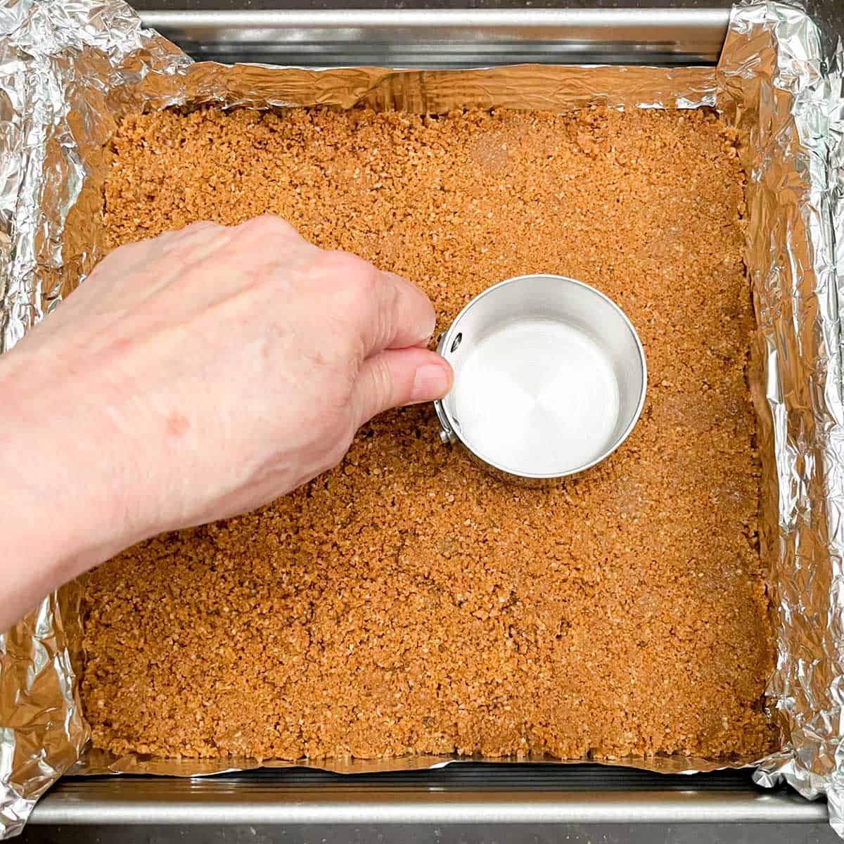 Using a flat bottom measuring cup to press the graham cracker crust down and flat.