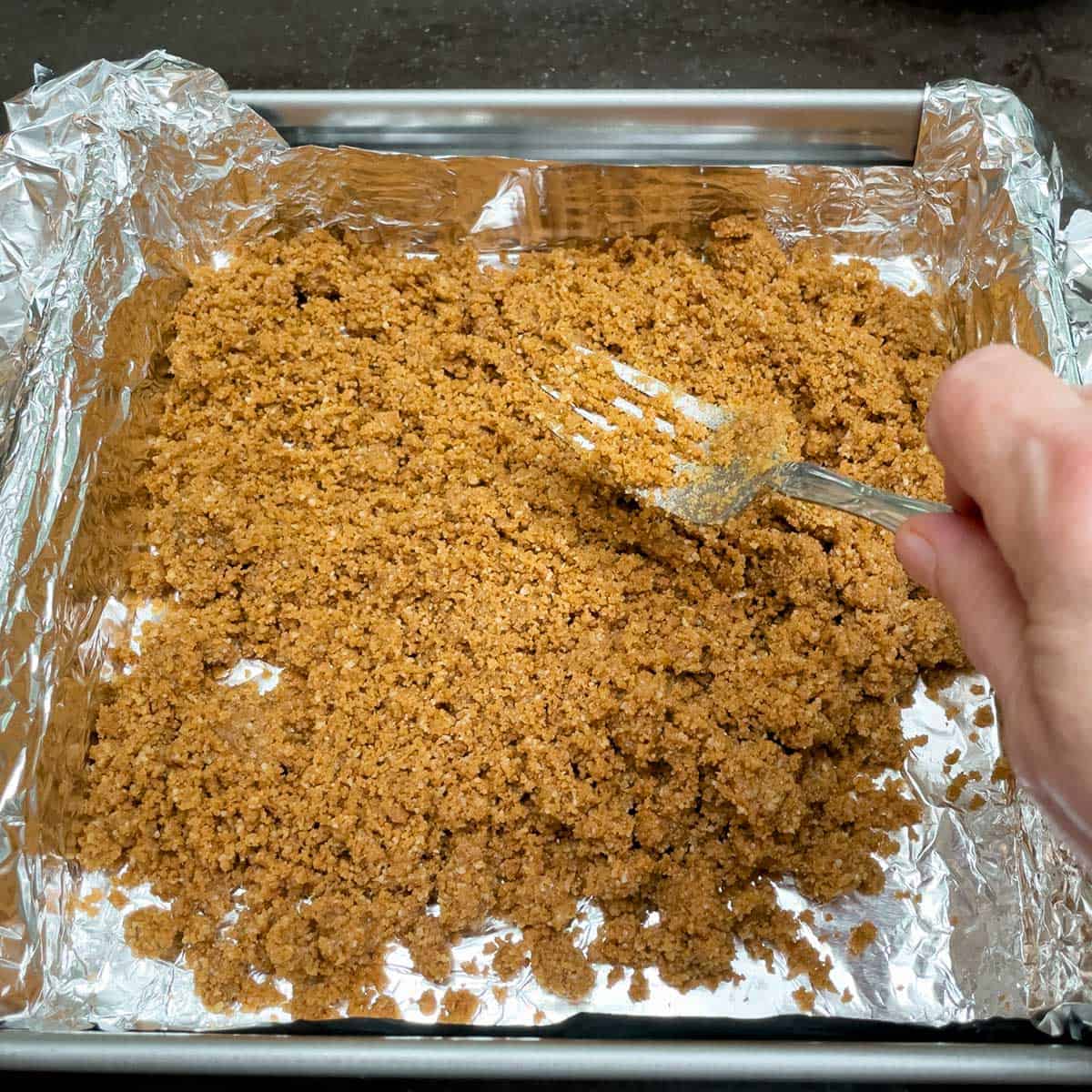 Pour the graham cracker crumble on to the tinfoil lined paned and spread it around the bottom.