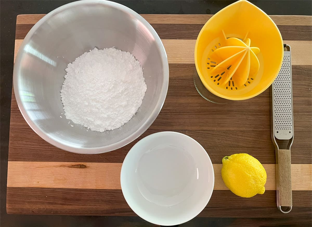 Powdered sugar in a mixing bowl and a lemon getting ready to be juiced and zested.