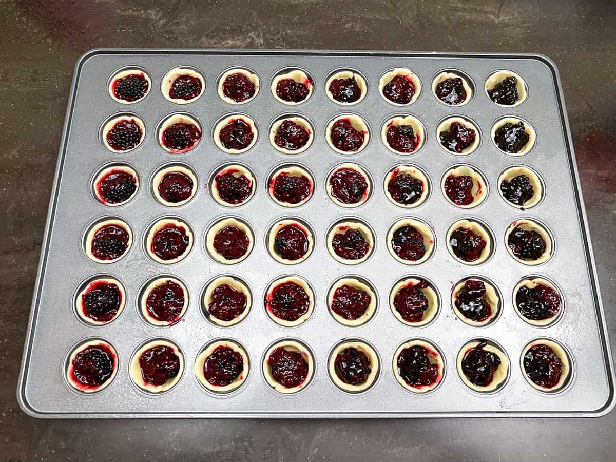 Mini muffin pan filled with blackberry cookie cups ready to be baked.