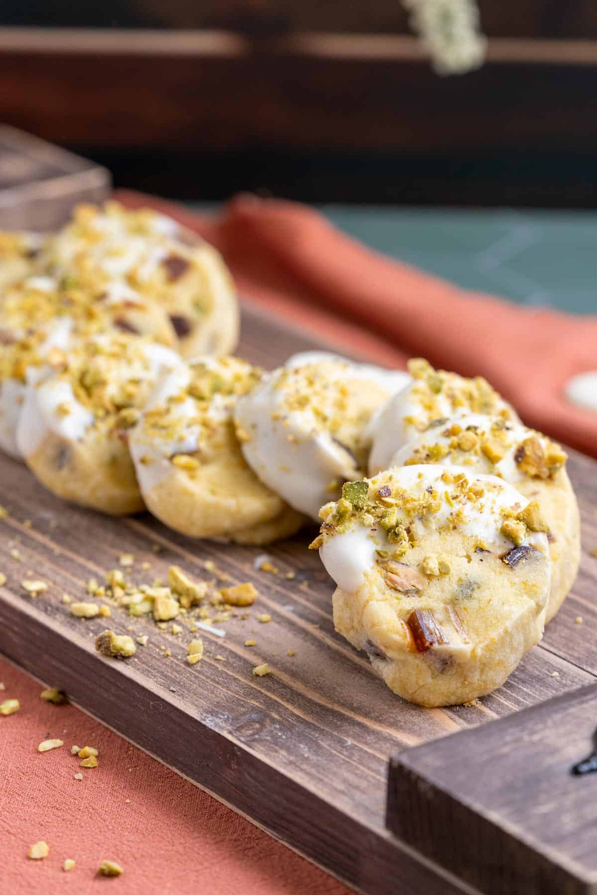 Pistachio date and orange cookies on a wooden plank.
