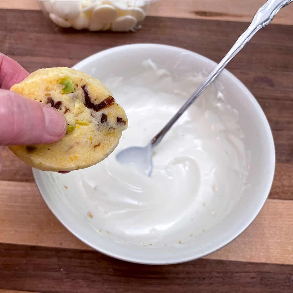 Holding the cookie in the middle to dip into the bowl of melted chocolate.