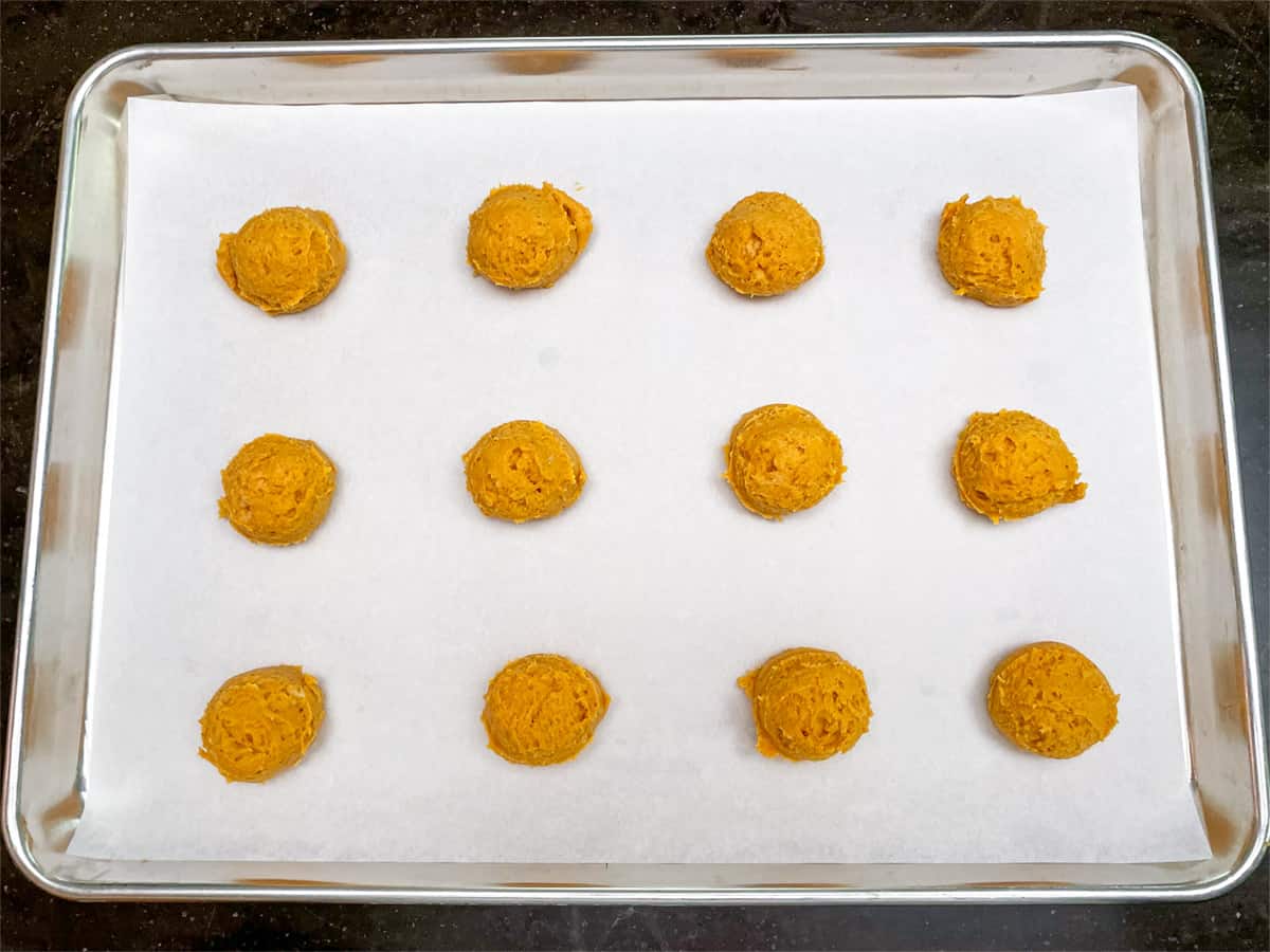 Pumpkin cookie dough scooped onto a parchment lined sheet pan.