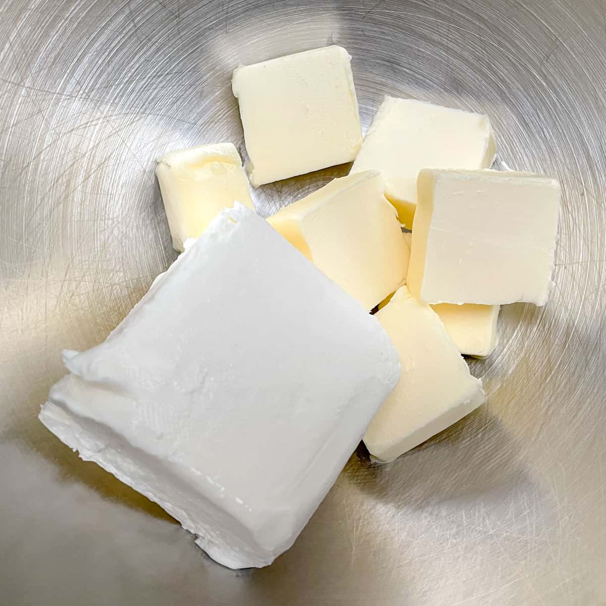 Cubed butter and a block of cream cheese in a mixer bowl.