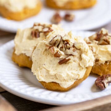 All about pumpkin cookies on a plate. Cookie with frosting and chopped pecans on top.