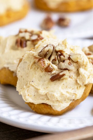 All about pumpkin cookies on a plate. Cookie with frosting and chopped pecans on top.