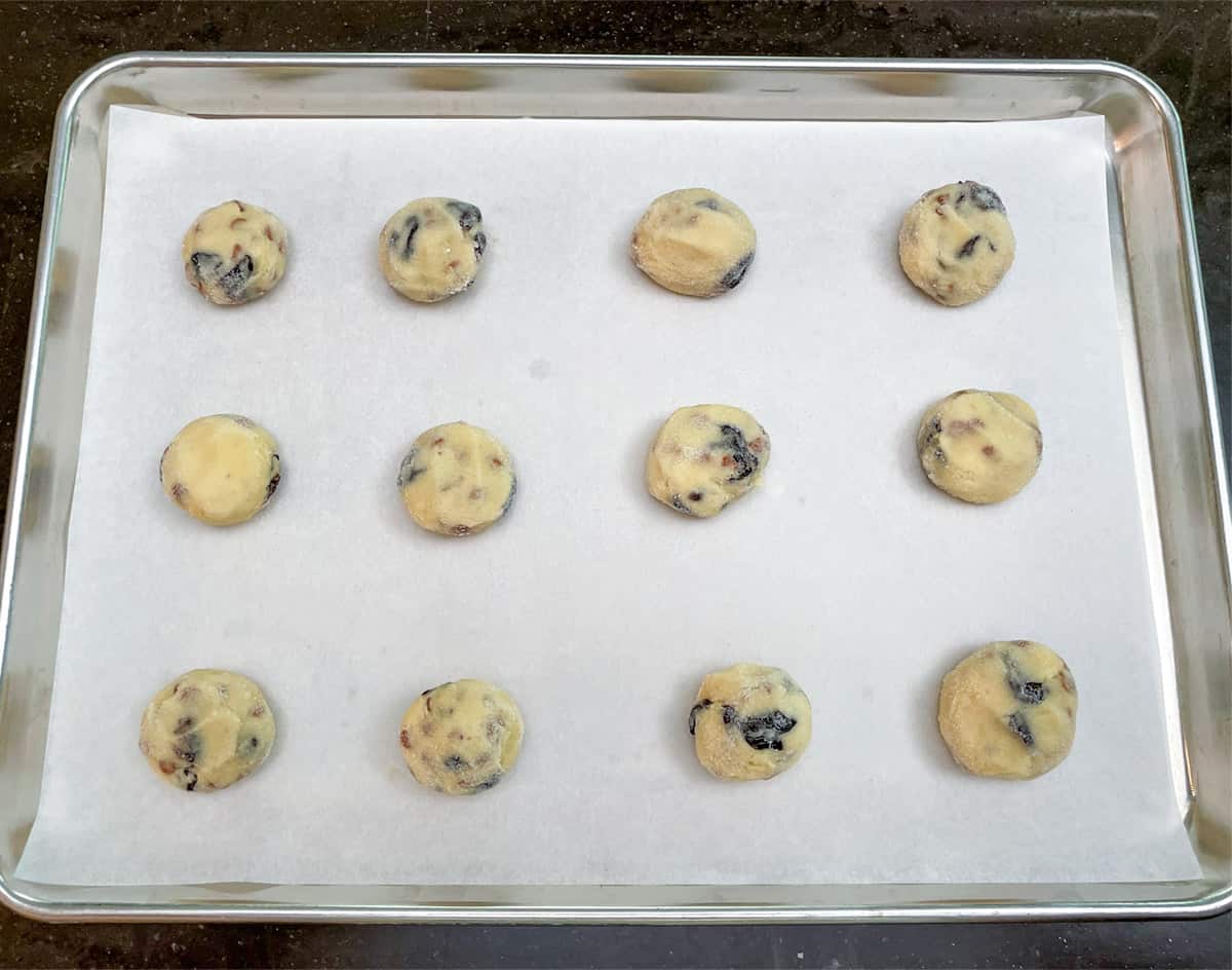 12 cookie balls that have been flatten slightly on a parchment paper lined cookie sheet pan.