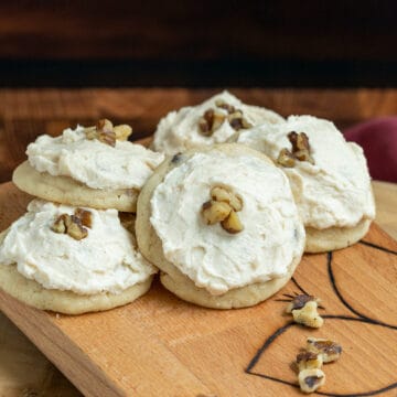 Five Applesauce and Walnut cookies on a wooden board with icing and 3 chopped walnuts on top of the icing.