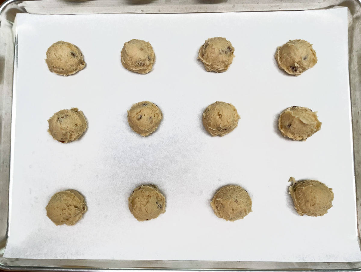 Scooped applesauce and walnut cookie dough on a parchment lined cookie sheet pan.