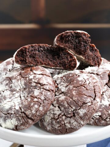 Mexican chocolate Crinkle Cookies laying on a plate with the top cookie split in half to see the rich chocolate inside.