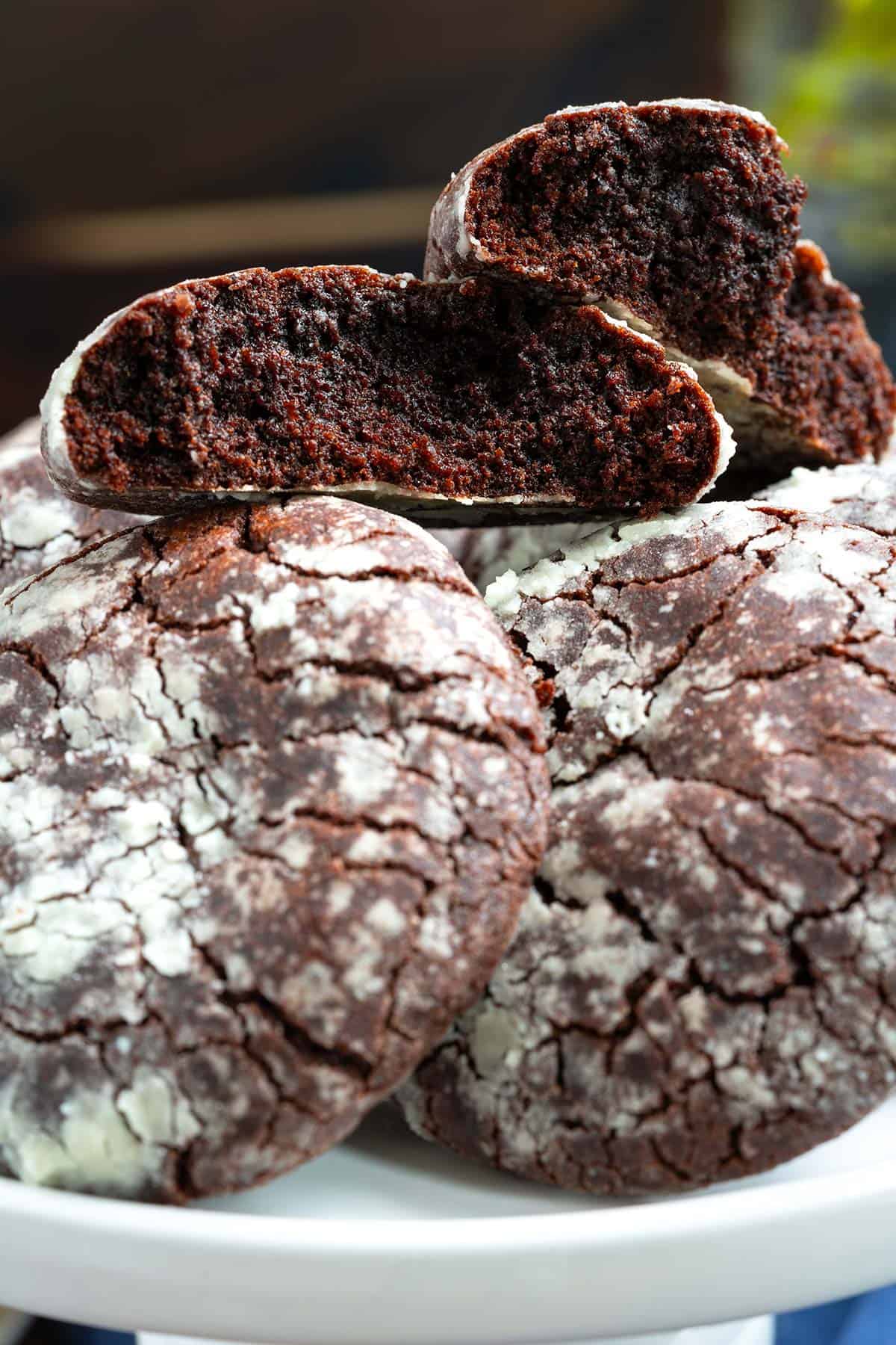 Full photo of the Mexican chocolate Crinkle Cookies laying on a plate with the top cookie split in half to see the rich chocolate inside.