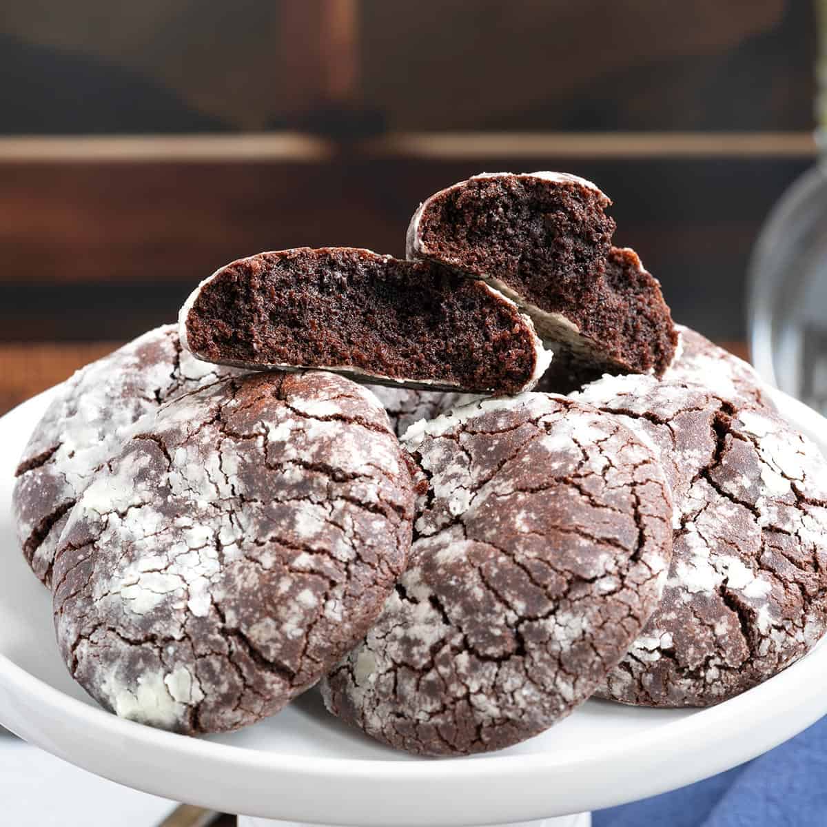 Mexican chocolate Crinkle Cookies laying on a plate with the top cookie split in half to see the rich chocolate inside.