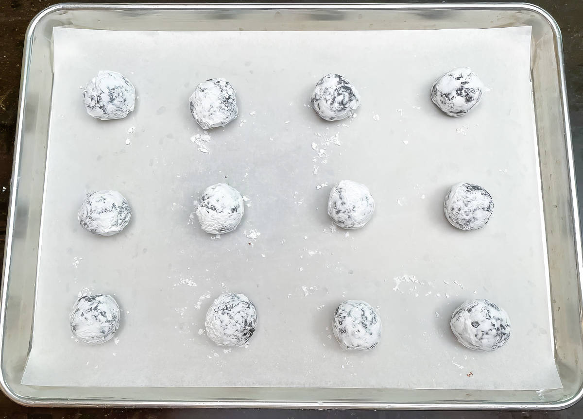 Twelve coated cookie balls on a parchment paper lined pan ready for the oven.