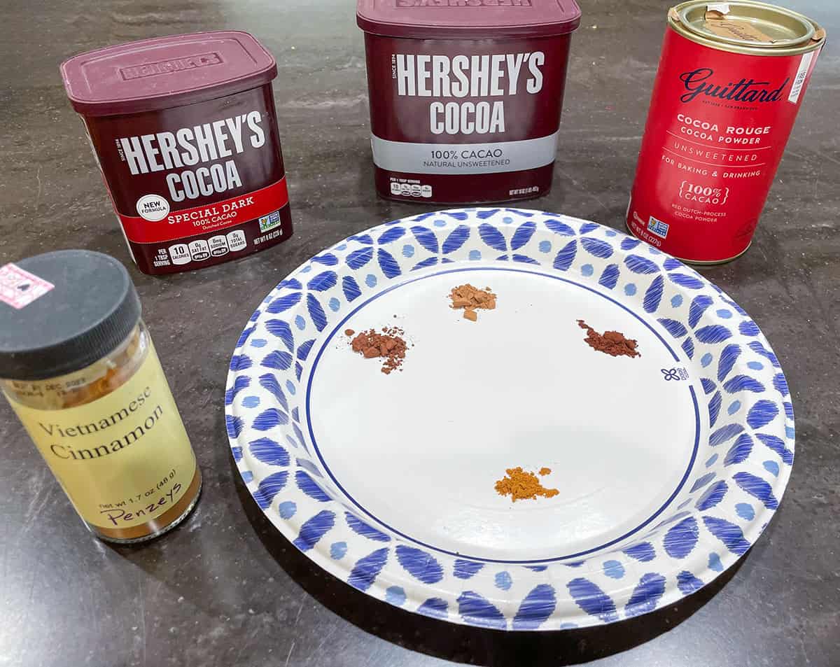 Three cocoa cans with samples on a plate for taste tasting. Also a jar of cinnamon to go along with it.