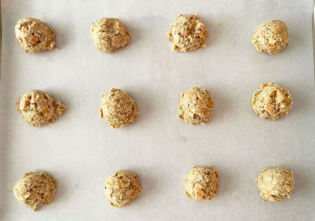 Twelve scooped cookie dough balls on a parchment lined cookie sheet pan.