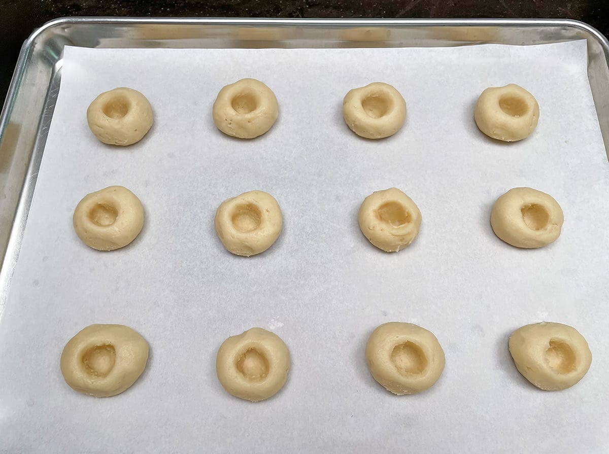 Twelve cookie balls on a parchment lined sheet pan that have well for adding the fig and walnut filling.