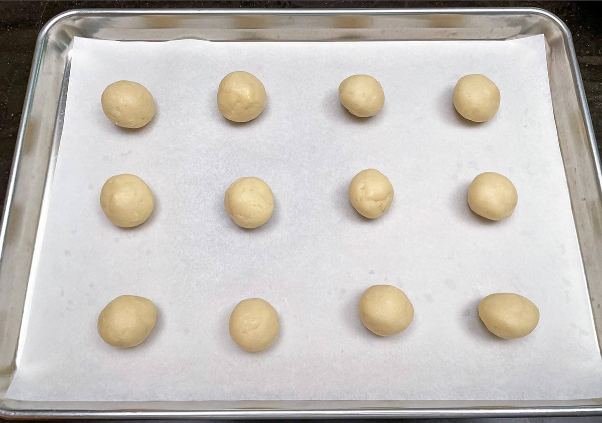 Twelve cookie scoops made into round balls and sitting on a parchment-lined cookie sheet pan.