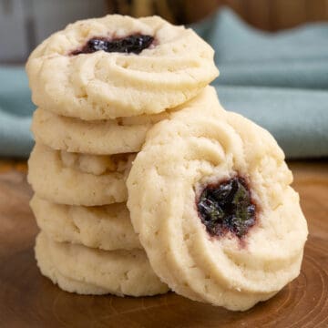 A stack of five shortbread cookies with jam and one leaning against the stack.