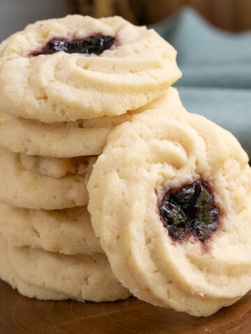 A stack of five shortbread cookies with jam and one leaning against the stack.