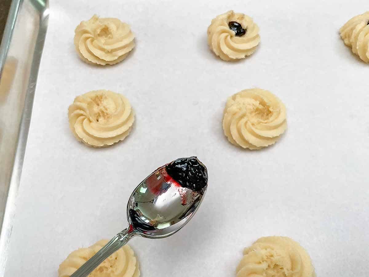 Showing on a teaspoon the small amount of jam that is needed to fill the holes in the rosette shaped cookies.