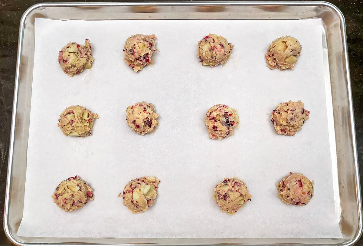 Scooped cookie dough on a parchment lined cookie sheet pan.
