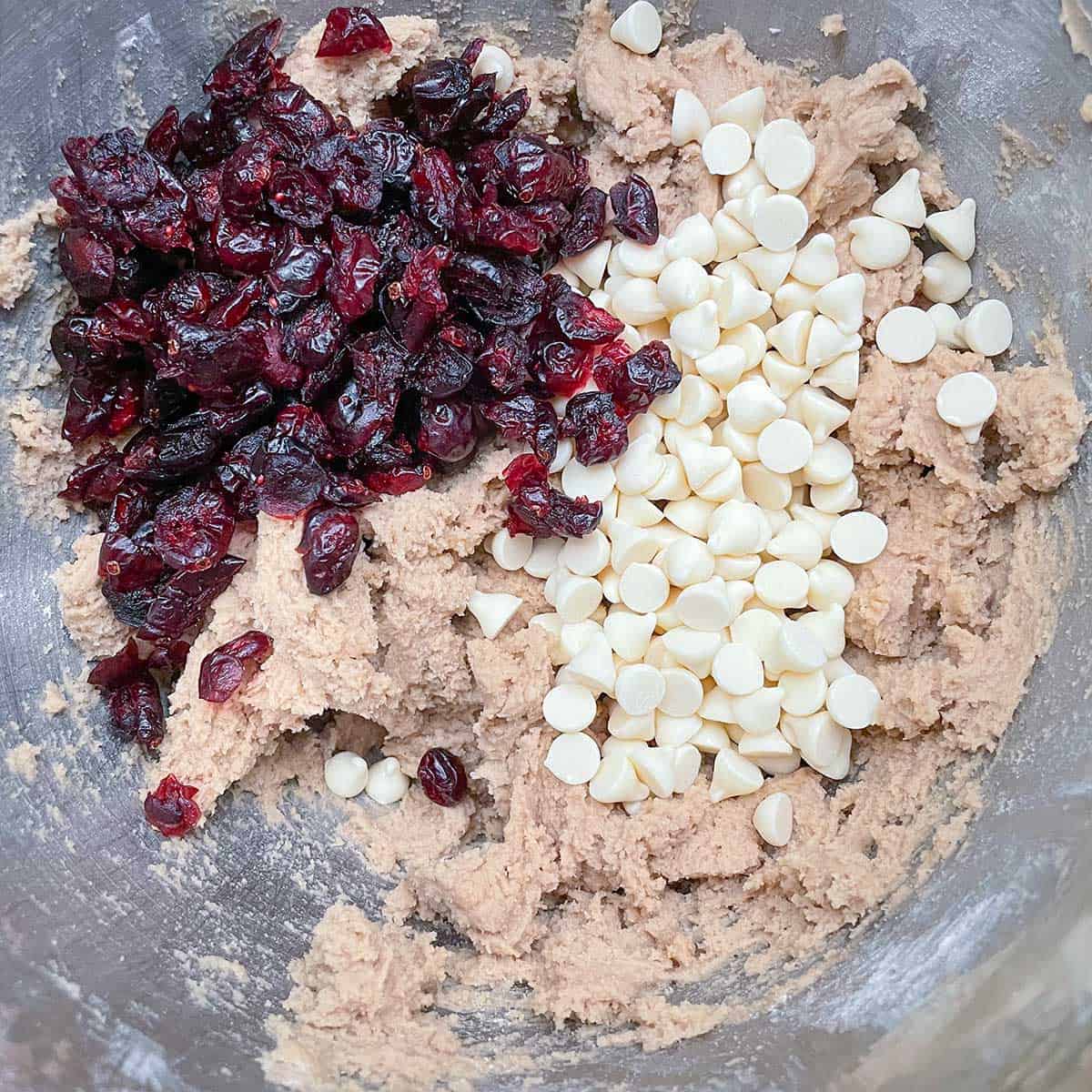 Cookie dough with dried cranberries and white chocolate chips on top, ready to be mixed into the dough.