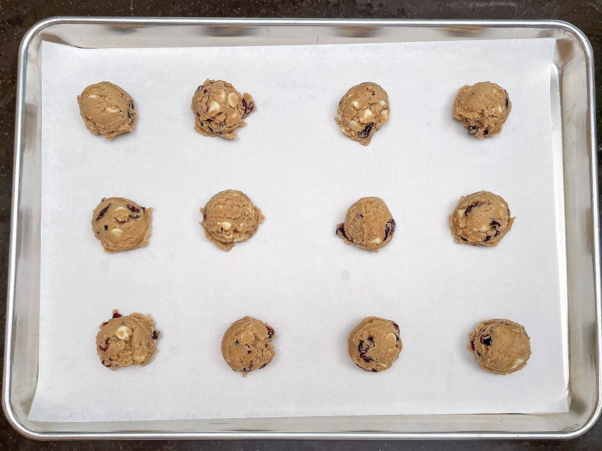 Parchment-lined sheet pan with scooped cranberry and white chocolate cookie dough.