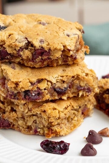 Cut cranberry cinnamon chocolate chip bars sitting stacked on a plate feature photo.