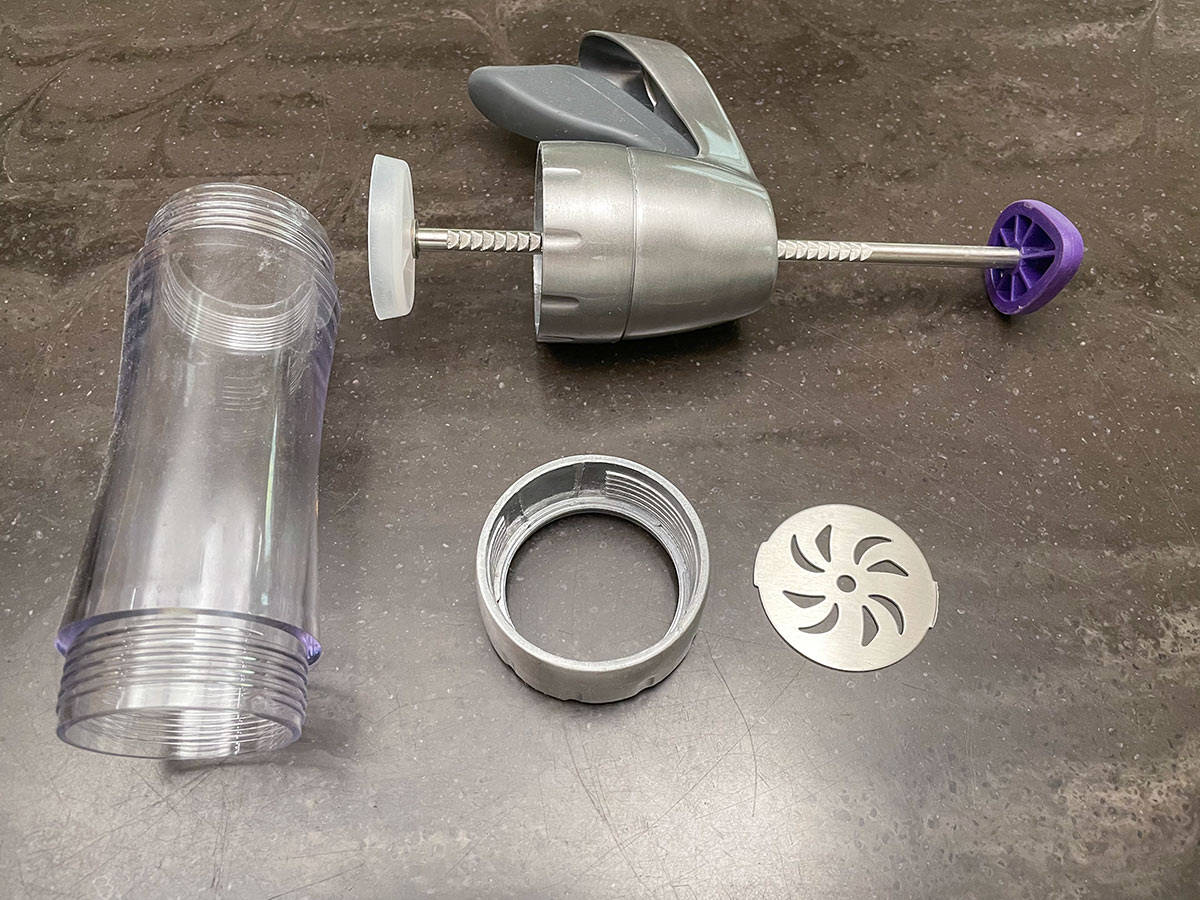 Parts of a cookie press taken apart. There is the barrel, disk, screw mount to hold the disk and the trigger.