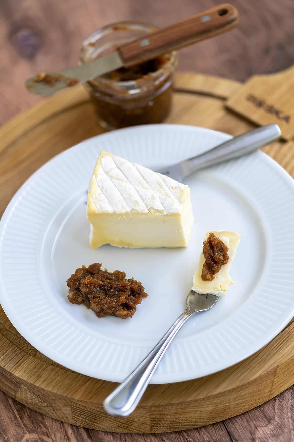 A piece of Brie cheese on a plate with fig filling on top of the Brie.