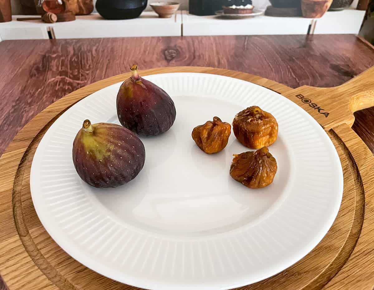 Two fresh figs and three dried figs on a plate.