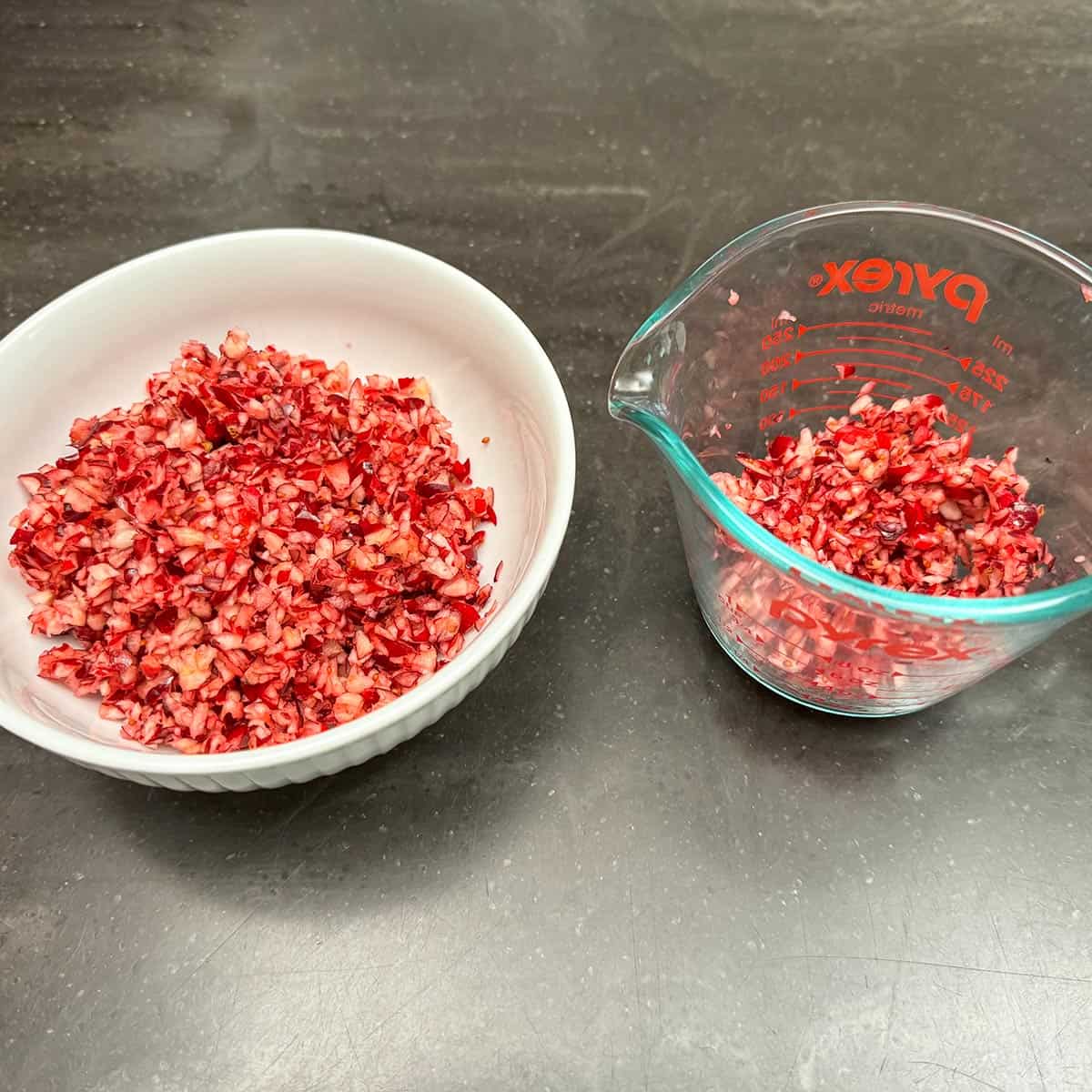 A bowl and a measuring cup of chopped cranberries. One for the cookie and the other for the topping on on the icing.