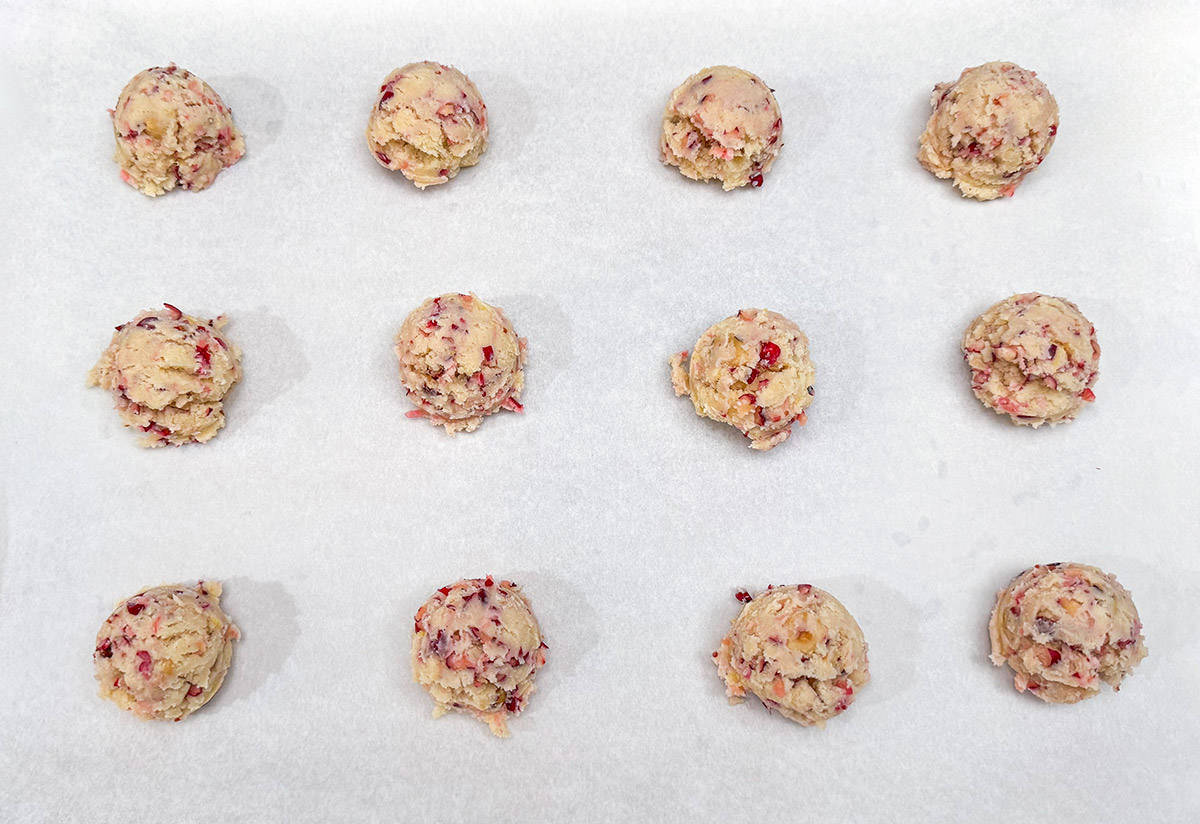 Scooped chilled cranberry cookie dough that is placed onto a parchment lined sheet pan.