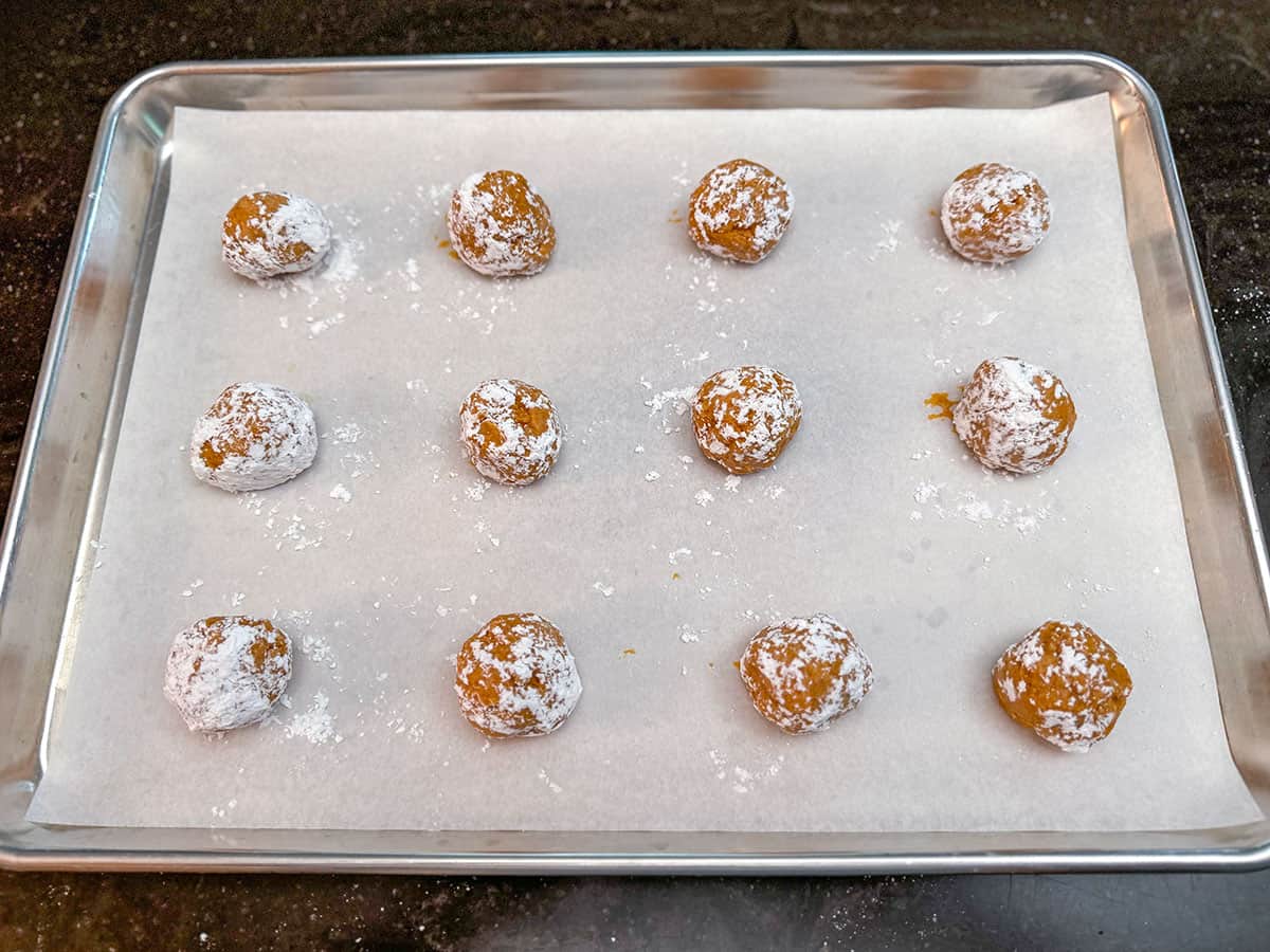 Scooped cookie balls rolled in powdered sugar sitting on a parchment-lined sheet pan.