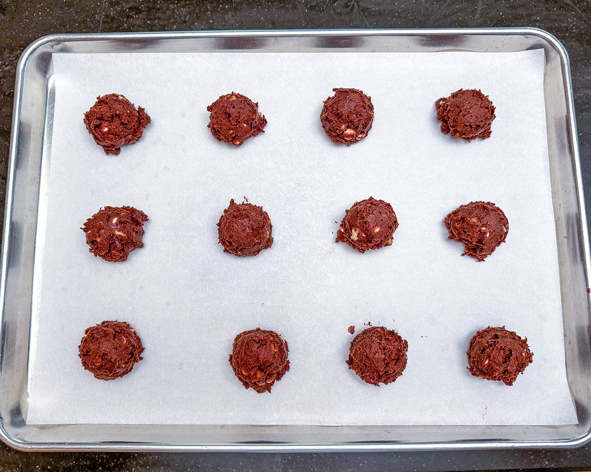 Scooped chocolate cookies on a parchment-lined sheet pan.