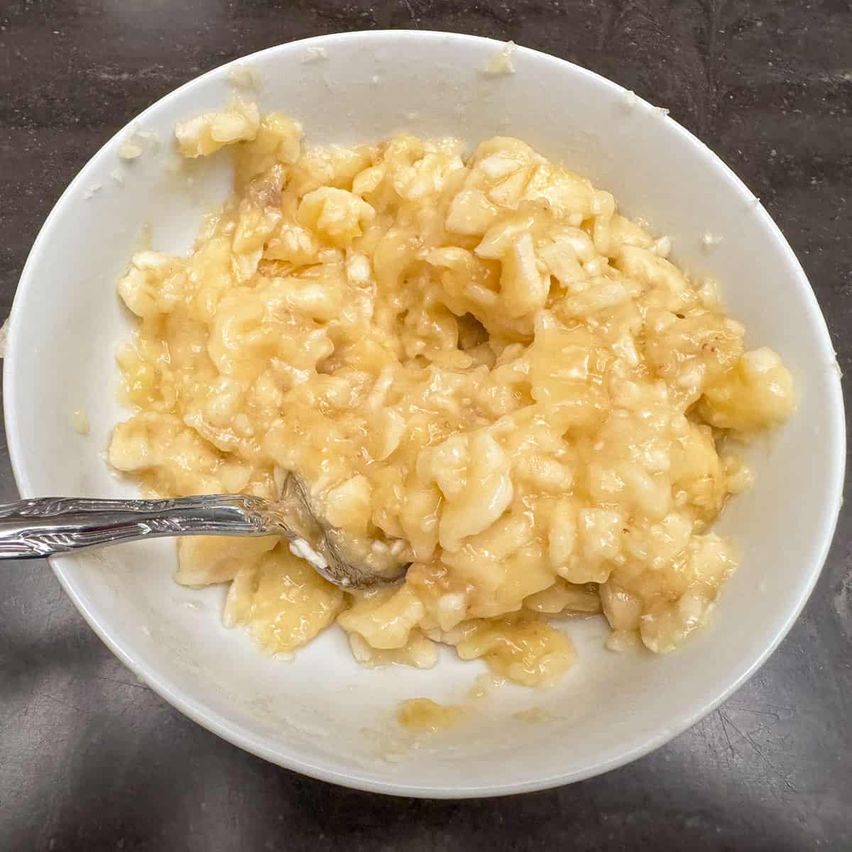 Banana slices mashed up with a fork in a small bowl.